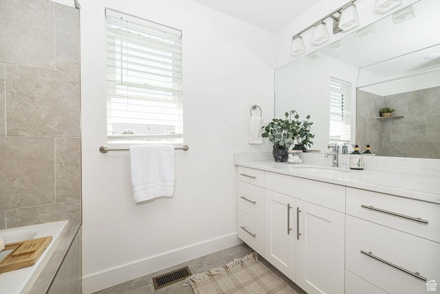 bathroom featuring vanity, a tile shower, baseboards, visible vents, and a bath