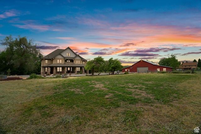 back of house at dusk with a yard, covered porch, an outbuilding, a garage, and a pole building