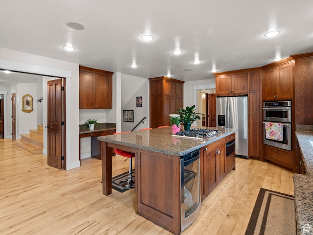 kitchen featuring dark stone counters, stainless steel appliances, light wood-style floors, a breakfast bar, and a kitchen island