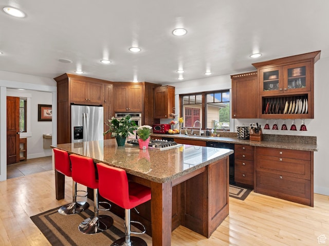 kitchen with light wood finished floors, a sink, a center island, a breakfast bar area, and appliances with stainless steel finishes