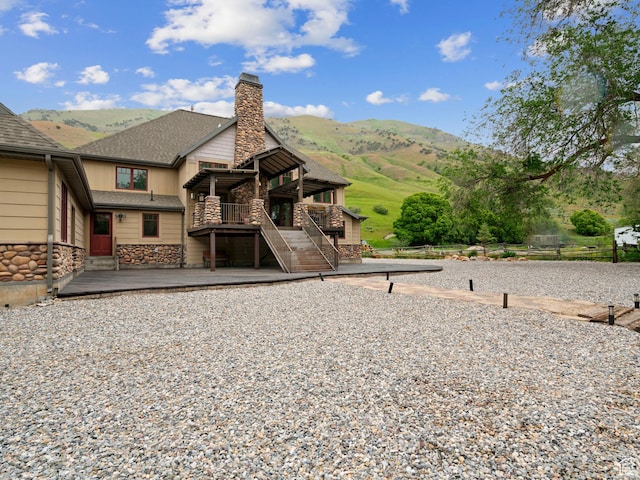 back of property featuring a chimney, a deck with mountain view, stairway, stone siding, and roof with shingles
