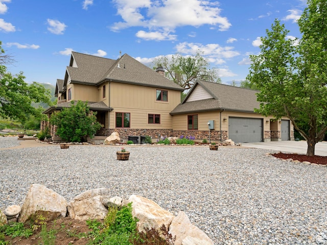 view of front of home featuring a chimney, a garage, stone siding, driveway, and roof with shingles