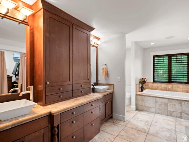full bath featuring toilet, double vanity, a sink, and tiled tub