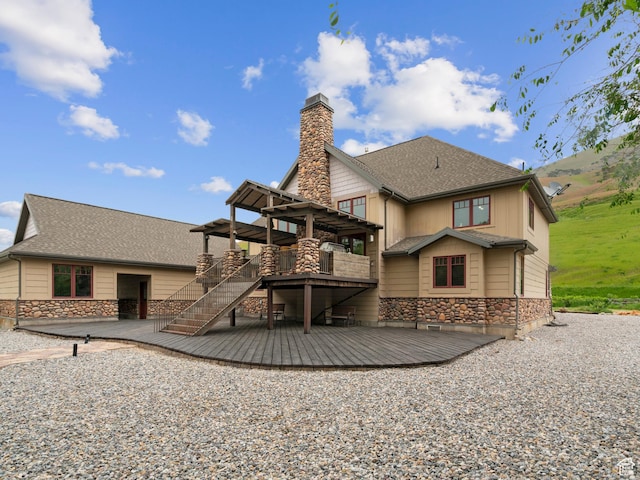 rear view of property with stone siding, a chimney, a deck, a shingled roof, and a pergola