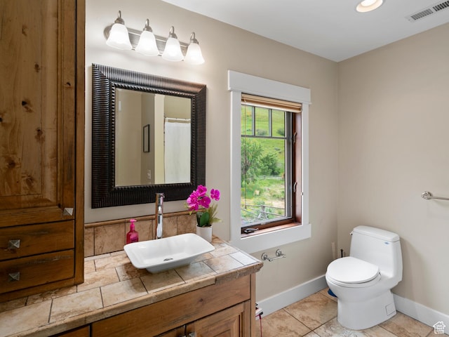 bathroom with toilet, visible vents, vanity, and baseboards