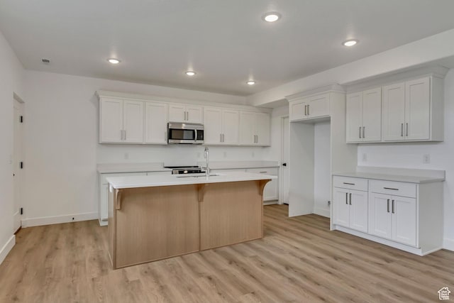 8077 N Bristle Cone Rd, Eagle Mountain, UT 84005 - kitchen with light countertops, stainless steel microwave, a sink, light wood-style flooring, and a kitchen island with sink