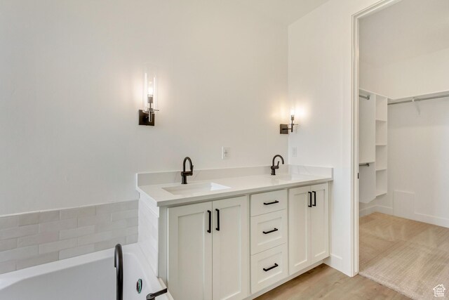 8077 N Bristle Cone Rd, Eagle Mountain, UT 84005 - bathroom featuring a spacious closet, a sink, a tub to relax in, and wood finished floors