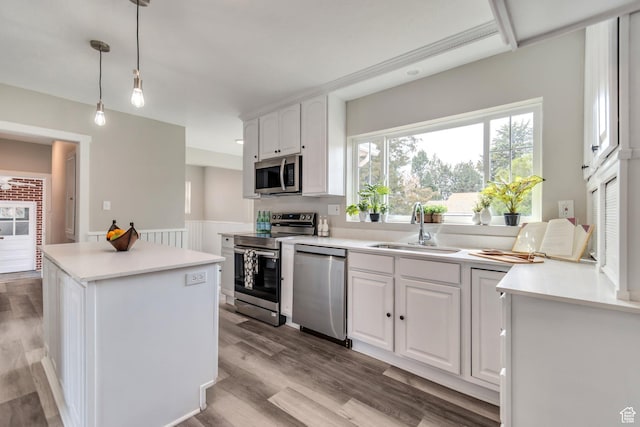 kitchen featuring wood finished floors, a kitchen island, appliances with stainless steel finishes, white cabinetry, and a sink