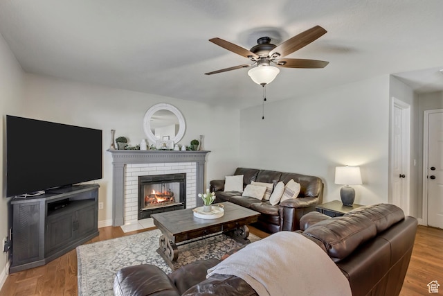 living room with a brick fireplace, baseboards, ceiling fan, and wood finished floors