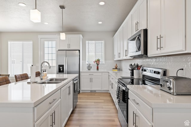 kitchen featuring tasteful backsplash, light wood-type flooring, a center island with sink, a sink, and appliances with stainless steel finishes