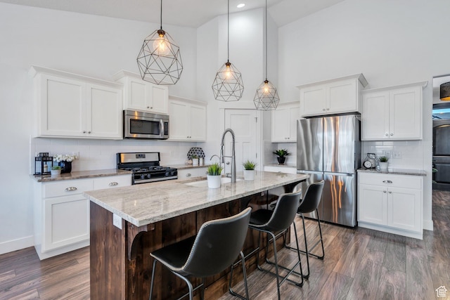 9844 N Faust Station Dr W, Eagle Mountain, UT 84005 - kitchen with a breakfast bar area, a center island with sink, stainless steel appliances, a towering ceiling, and dark wood-type flooring