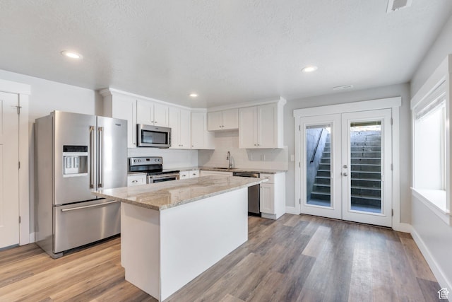 9844 N Faust Station Dr W, Eagle Mountain, UT 84005 - kitchen with white cabinets, stainless steel appliances, light wood-type flooring, light stone counters, and backsplash