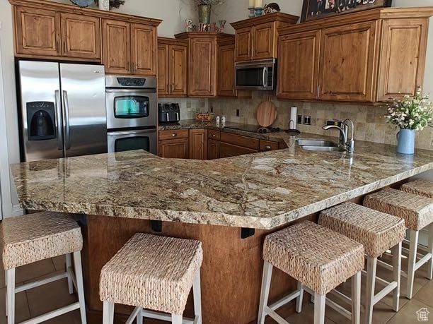 958 S Bridgecreek Ln, Layton, UT 84041 - kitchen with tasteful backsplash, light stone countertops, brown cabinets, a sink, and stainless steel appliances