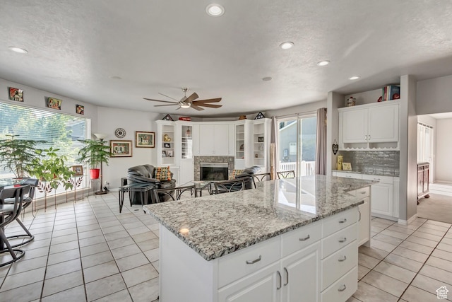 496 E Spruce Glen Rd, Murray, UT 84107 - kitchen featuring light tile patterned flooring, ceiling fan, a center island, a glass covered fireplace, and white cabinetry