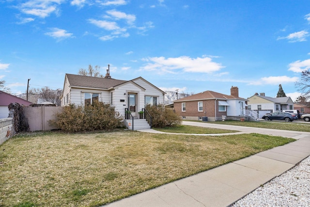 bungalow-style home with a residential view, concrete driveway, fence, and a front lawn