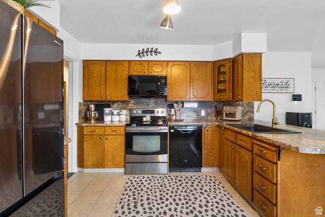kitchen with tasteful backsplash, a sink, black appliances, brown cabinetry, and light tile patterned floors