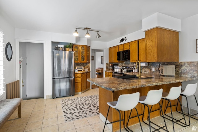 kitchen with a peninsula, brown cabinets, tasteful backsplash, appliances with stainless steel finishes, and light tile patterned floors
