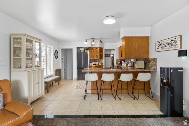 kitchen featuring tasteful backsplash, a sink, light tile patterned flooring, freestanding refrigerator, and a peninsula