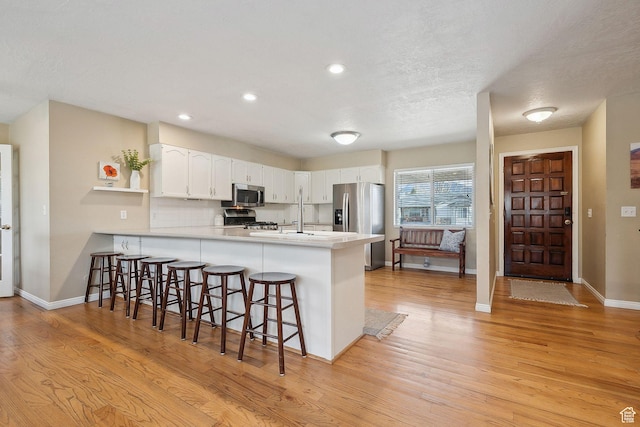 32 E 500 S, Midway, UT 84049 - kitchen featuring stainless steel appliances, a peninsula, light wood-type flooring, a breakfast bar area, and white cabinetry