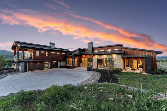 view of front of house featuring a standing seam roof, concrete driveway, a chimney, metal roof, and a garage
