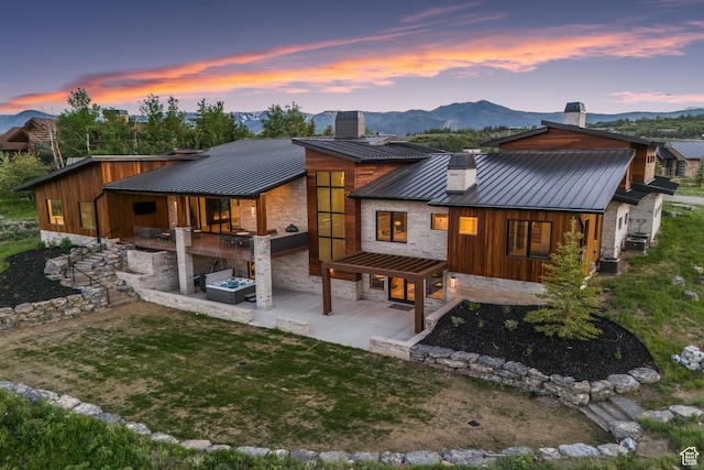 7290 Foxglove Ct, Park City, UT 84098 - back of house at dusk featuring a standing seam roof, a patio, stone siding, metal roof, and a chimney