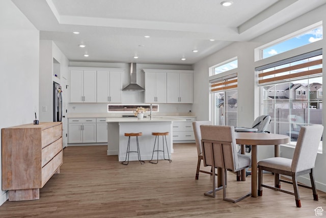 217 S Buckhorn Bath Ave W, Saratoga Springs, UT 84045 - kitchen with light countertops, a center island with sink, light wood finished floors, wall chimney range hood, and white cabinets