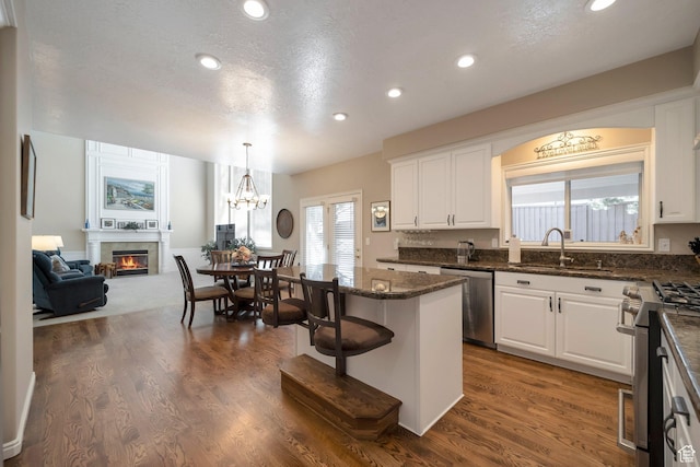 kitchen featuring white cabinetry, a sink, stainless steel appliances, and a glass covered fireplace