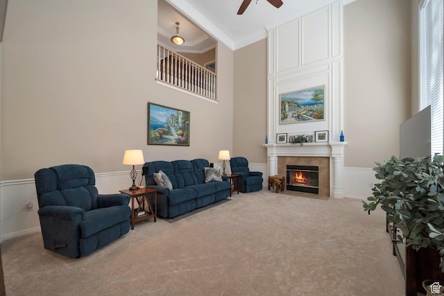 carpeted living room with a towering ceiling, crown molding, ceiling fan, and a tile fireplace