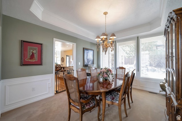 dining area with a tray ceiling, a chandelier, wainscoting, and light colored carpet