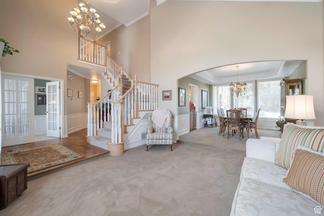 carpeted living area featuring stairs, a raised ceiling, arched walkways, a notable chandelier, and wainscoting