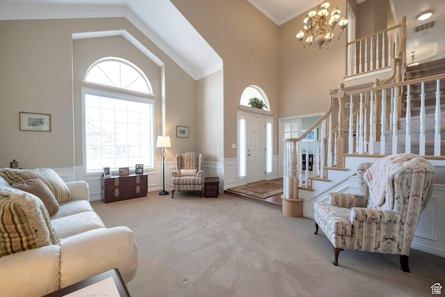 carpeted foyer entrance featuring a wainscoted wall, visible vents, ornamental molding, stairway, and an inviting chandelier