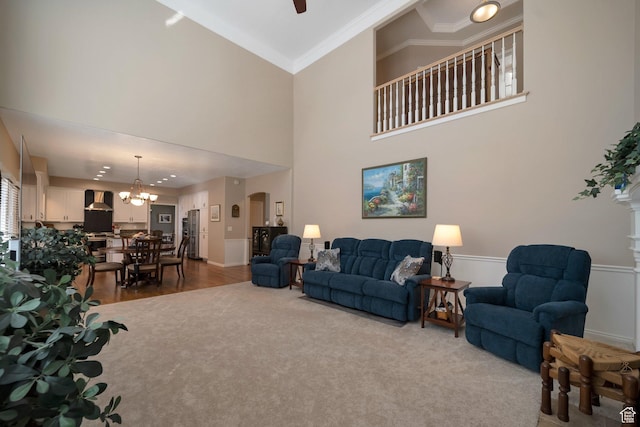 living room with ornamental molding, carpet flooring, arched walkways, and ceiling fan with notable chandelier