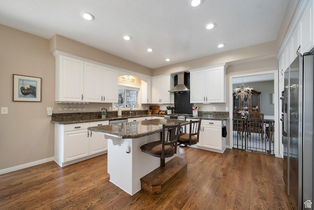 kitchen featuring dark wood-style flooring, white cabinets, stainless steel appliances, wall chimney exhaust hood, and a breakfast bar area