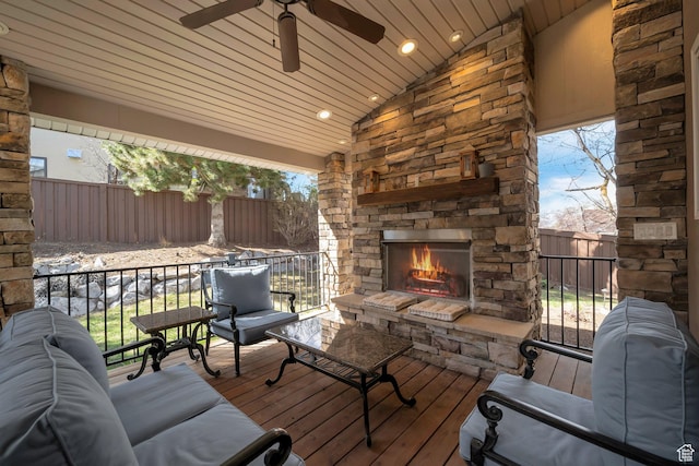 wooden terrace featuring an outdoor stone fireplace, fence, and a ceiling fan
