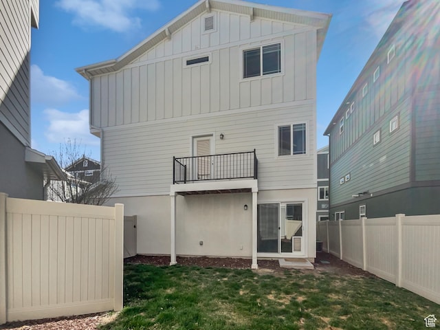 rear view of property featuring a balcony, a fenced backyard, board and batten siding, and a yard