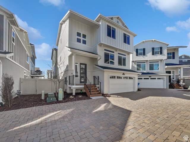 view of front of home with board and batten siding, decorative driveway, a garage, and fence