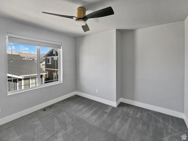 empty room with dark colored carpet, baseboards, ceiling fan, and visible vents