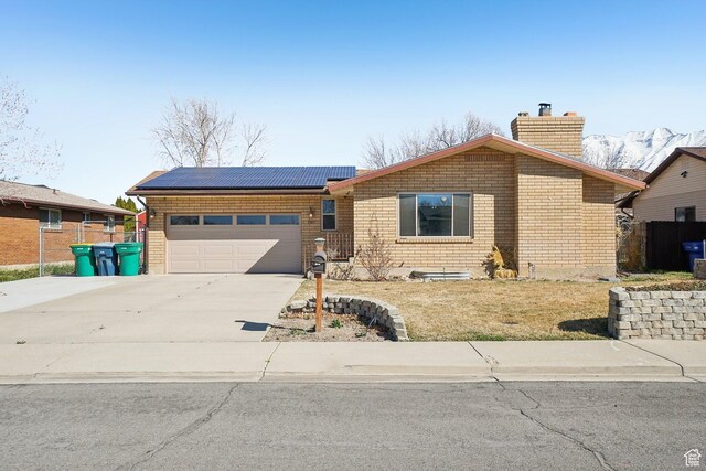 ranch-style home with concrete driveway, fence, solar panels, a garage, and a chimney