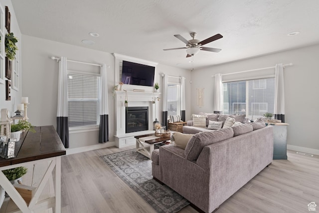 7016 N Amber Mead Ave, Eagle Mountain, UT 84005 - living area featuring a textured ceiling, baseboards, ceiling fan, light wood-style floors, and a glass covered fireplace