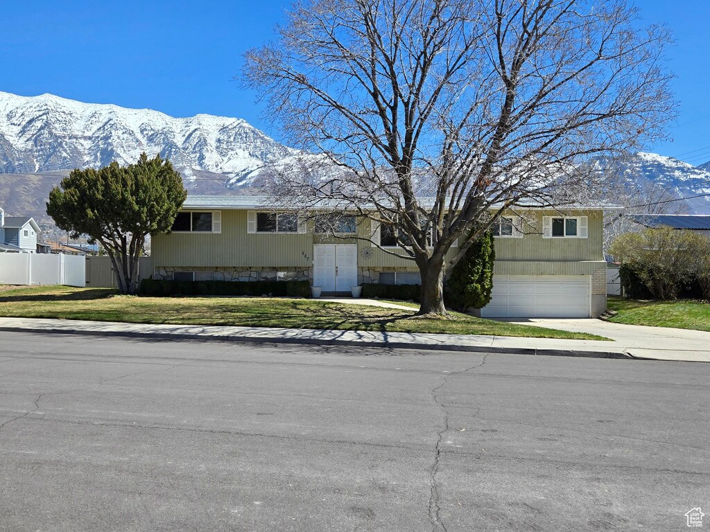 view of front of house featuring a mountain view, driveway, fence, an attached garage, and a front yard