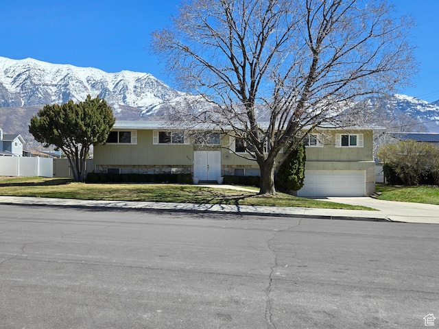 view of front of home with a mountain view, an attached garage, fence, concrete driveway, and a front lawn