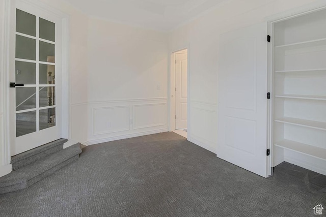 interior space featuring dark carpet, a decorative wall, and wainscoting