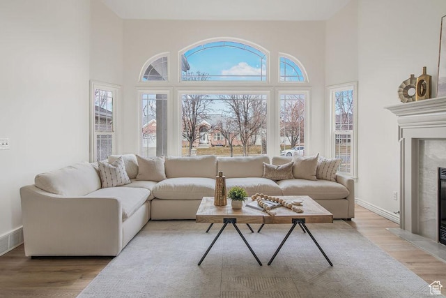 living area featuring a fireplace, high vaulted ceiling, light wood-style flooring, and baseboards