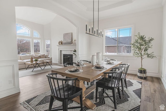 dining room with wood finished floors, arched walkways, a fireplace, and a decorative wall