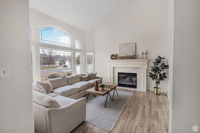living area with light wood-style floors, a tiled fireplace, and high vaulted ceiling