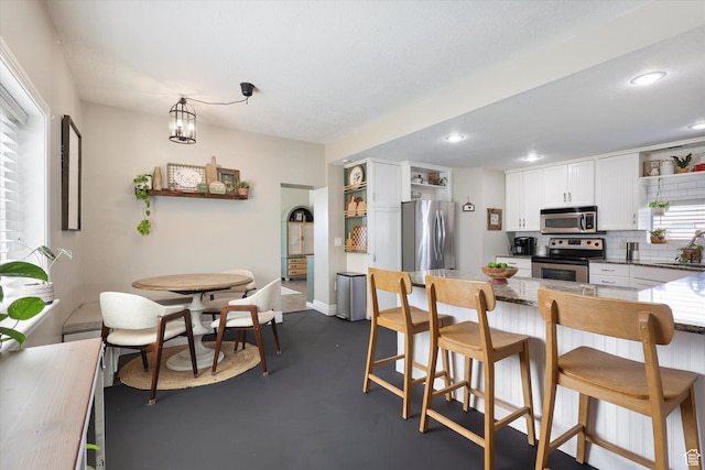 kitchen featuring white cabinets, a kitchen bar, stainless steel appliances, tasteful backsplash, and open shelves