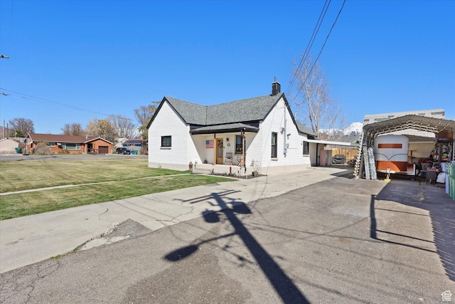 view of front facade with a front lawn, a detached carport, a chimney, and aphalt driveway