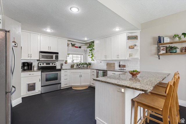 kitchen featuring a sink, open shelves, white cabinetry, appliances with stainless steel finishes, and a peninsula