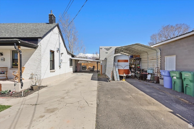 view of side of property featuring driveway, a chimney, brick siding, and a carport