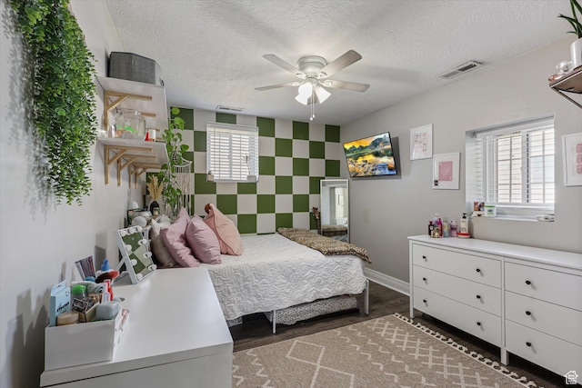 bedroom with an accent wall, wood finished floors, a textured ceiling, baseboards, and visible vents